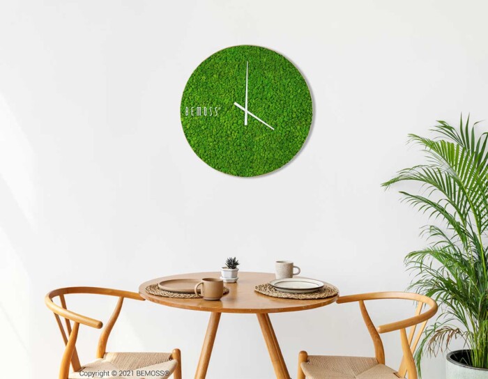eine Uhr an der Wand über einem Tisch mit Stühlen und einer Topfpflanze in der Ecke, moosbild, mooswand, moos pflanzen, moos, moos deko, moos art