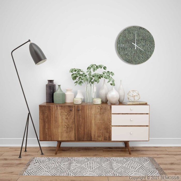 eine weiße Wand mit einer Uhr und einem Holzschrank mit Vasen und Pflanzen darauf und einem Teppich, moosbild, mooswand, moos pflanzen, moos, moos deko, moos art