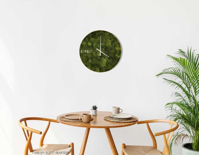 Ein Tisch mit zwei Stühlen und einer Uhr an der Wand darüber, auf der steht, dass die Zeit 4 Uhr ist, moosbild, mooswand, moos pflanzen, moos, moos deko, moos art