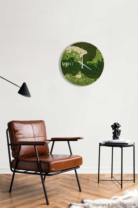 ein Stuhl und ein Tisch in einem Raum mit einer Uhr an der Wand darüber und einem Tisch mit einer Lampe darauf, moosbild, mooswand, moos pflanzen, moos, moos deko, moos art