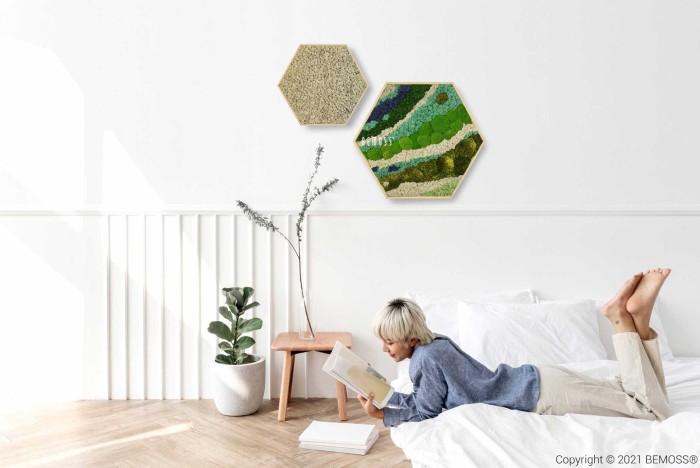Eine Frau liegt auf einem Bett und liest ein Buch in einem weißen Raum mit einem sechseckigen Wandbehang, moosbild, mooswand, moos pflanzen, moos, moos deko, moos art