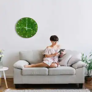 žena sediaca na gauči s knihou v ruke a hodinami na stene za ňou machovy obraz, stabilizovany mach, machová stena, machová dekorácia